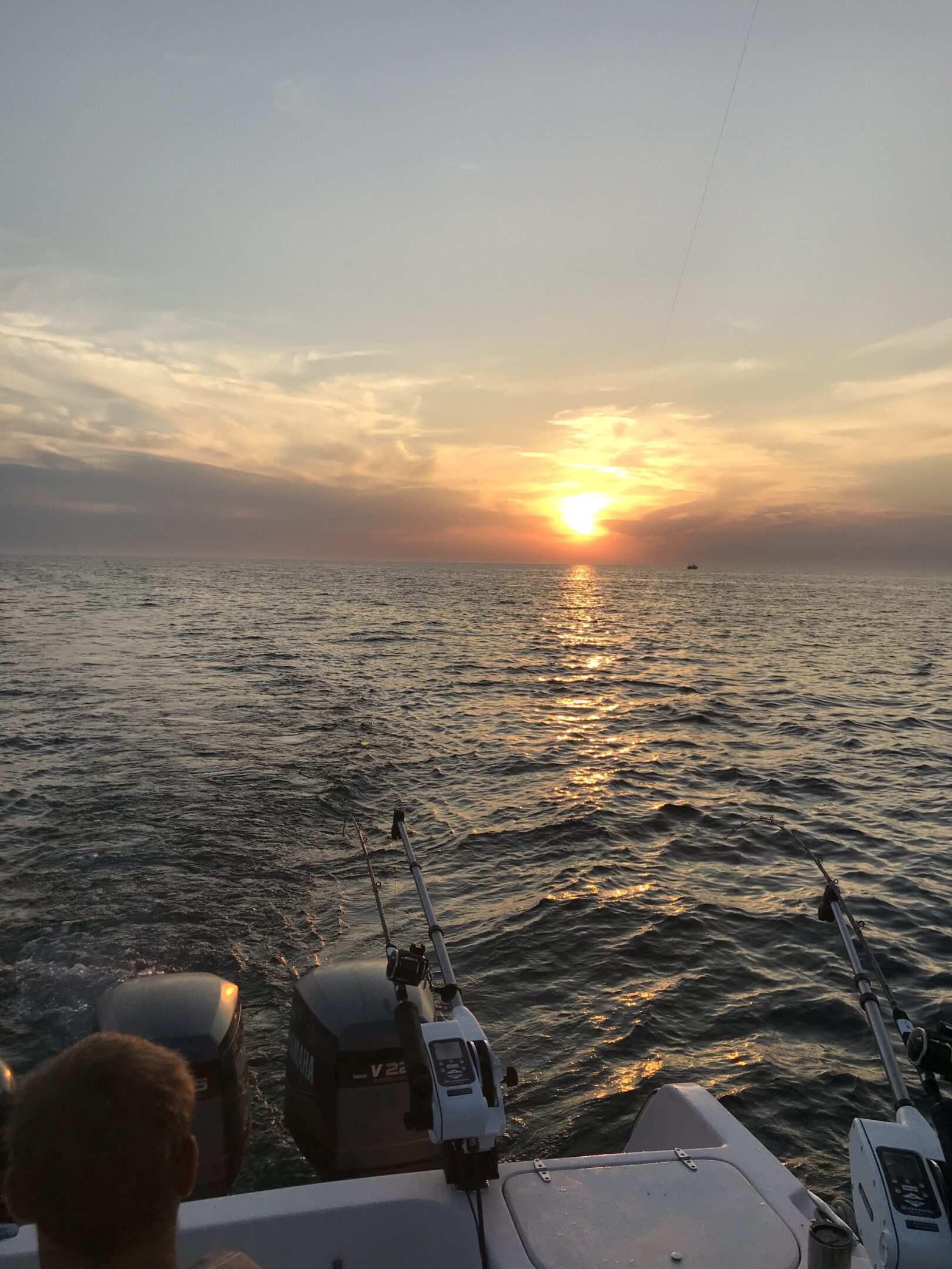Sunset over a calm sea with fishing rods on a boat.