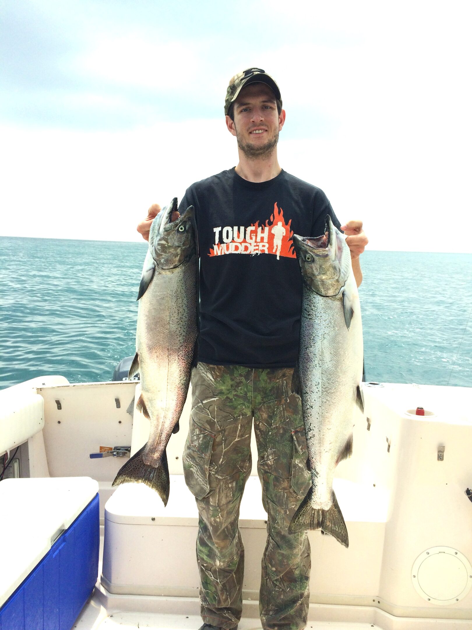 A man holding two large fish on a boat in the ocean.
