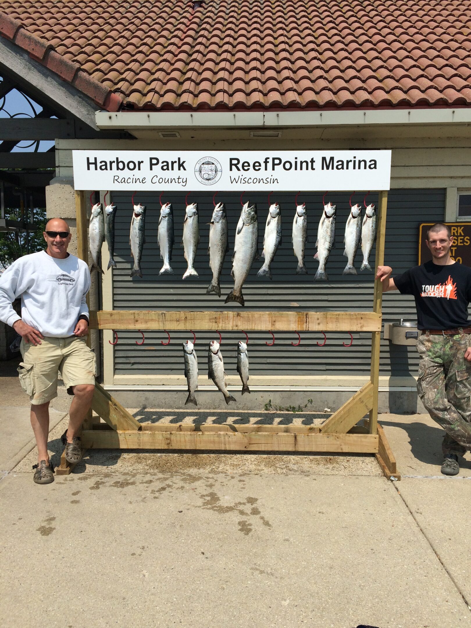 Two men posing by a fish display board at Harbor Park and Reef Point Marina.