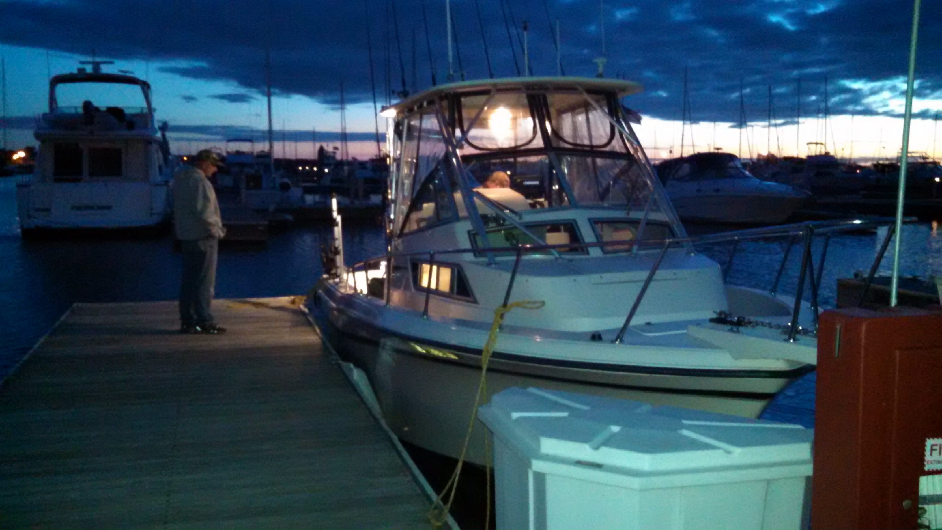 A boat docked at a marina during twilight with a cloudy sky.