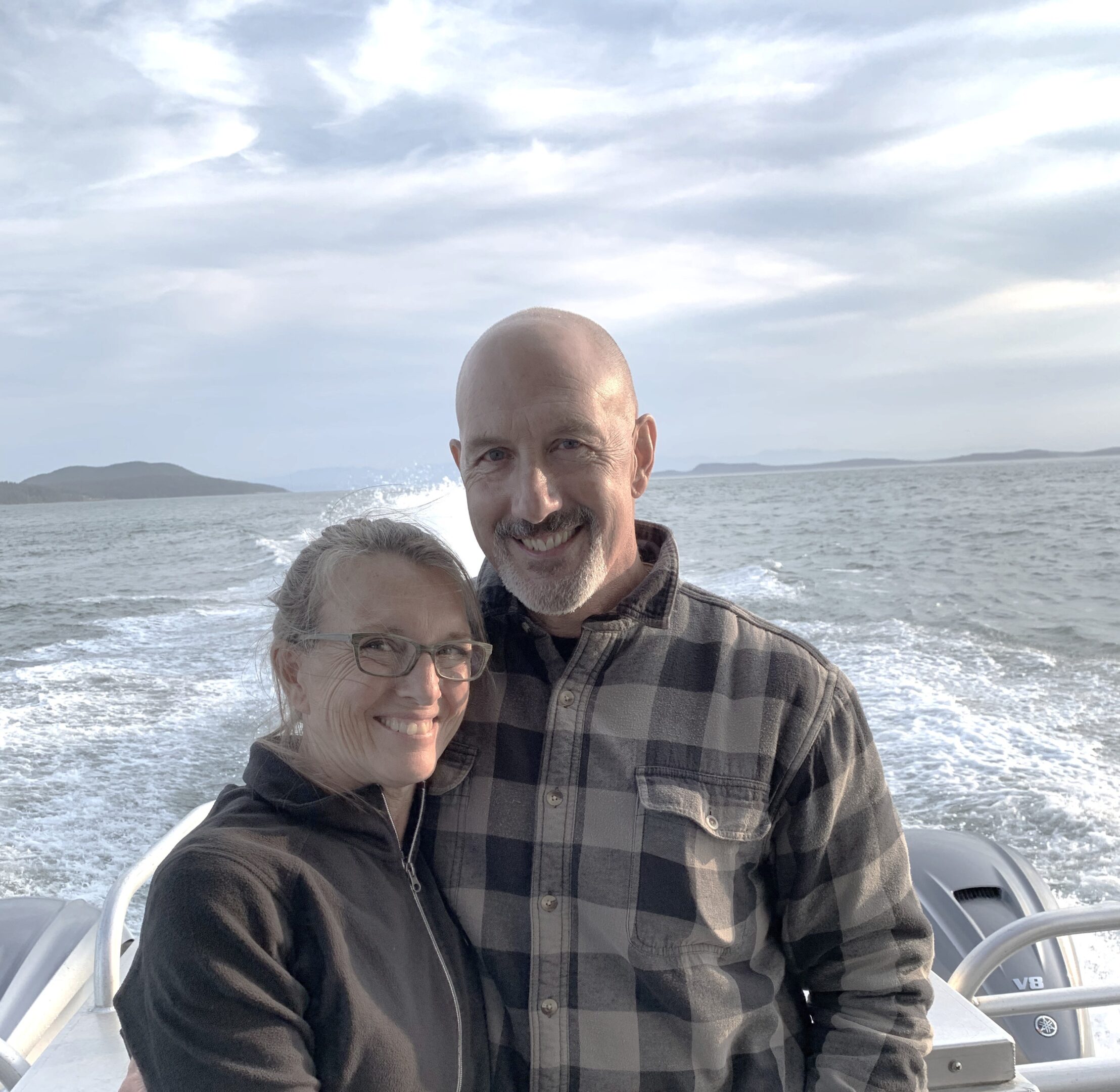 A smiling couple posing on a boat with the ocean in the background.