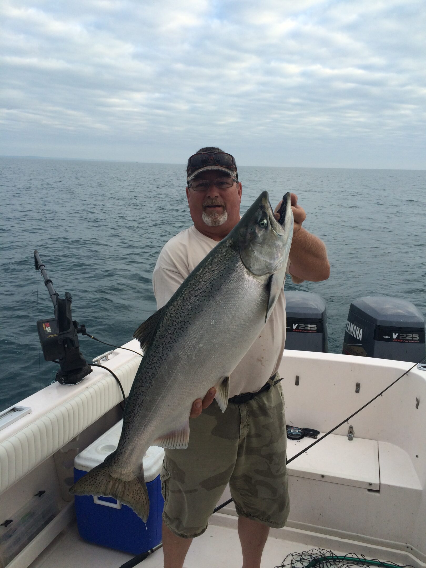 Man holding a large fish on a boat under cloudy skies.