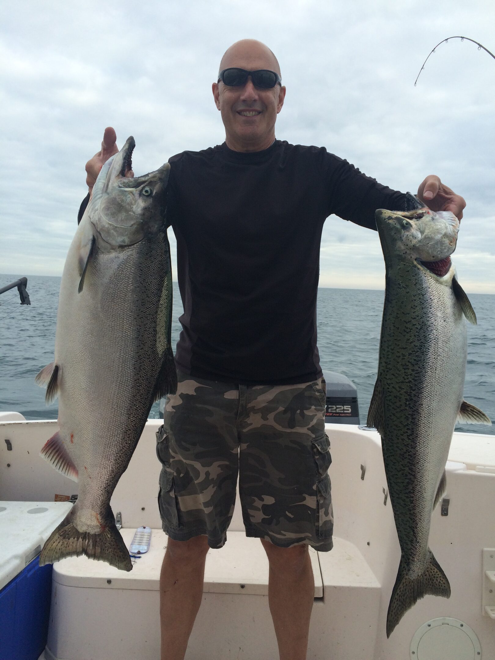 Man holding two large fish on a boat by the sea.