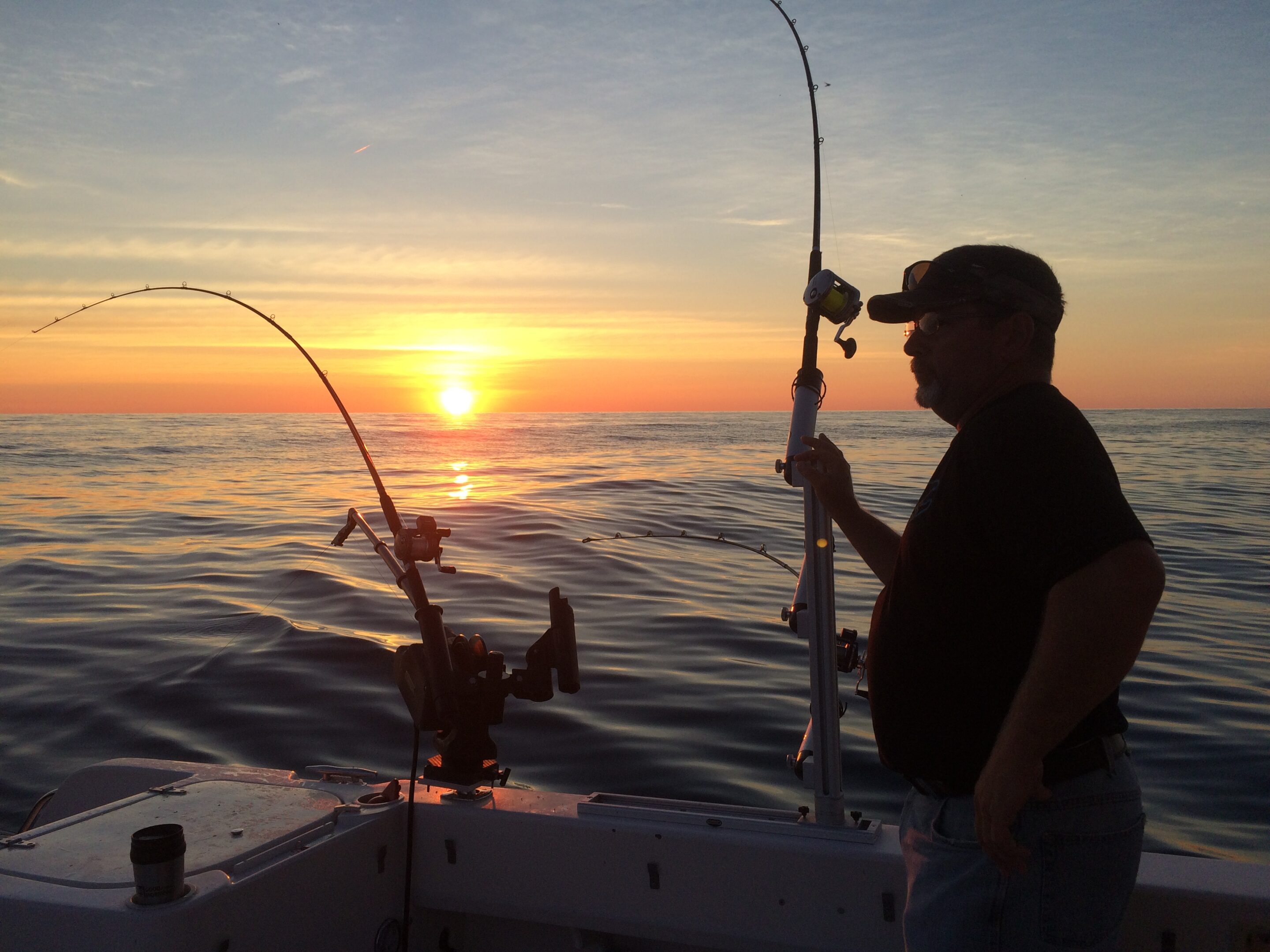 Man fishing on a boat during sunset.