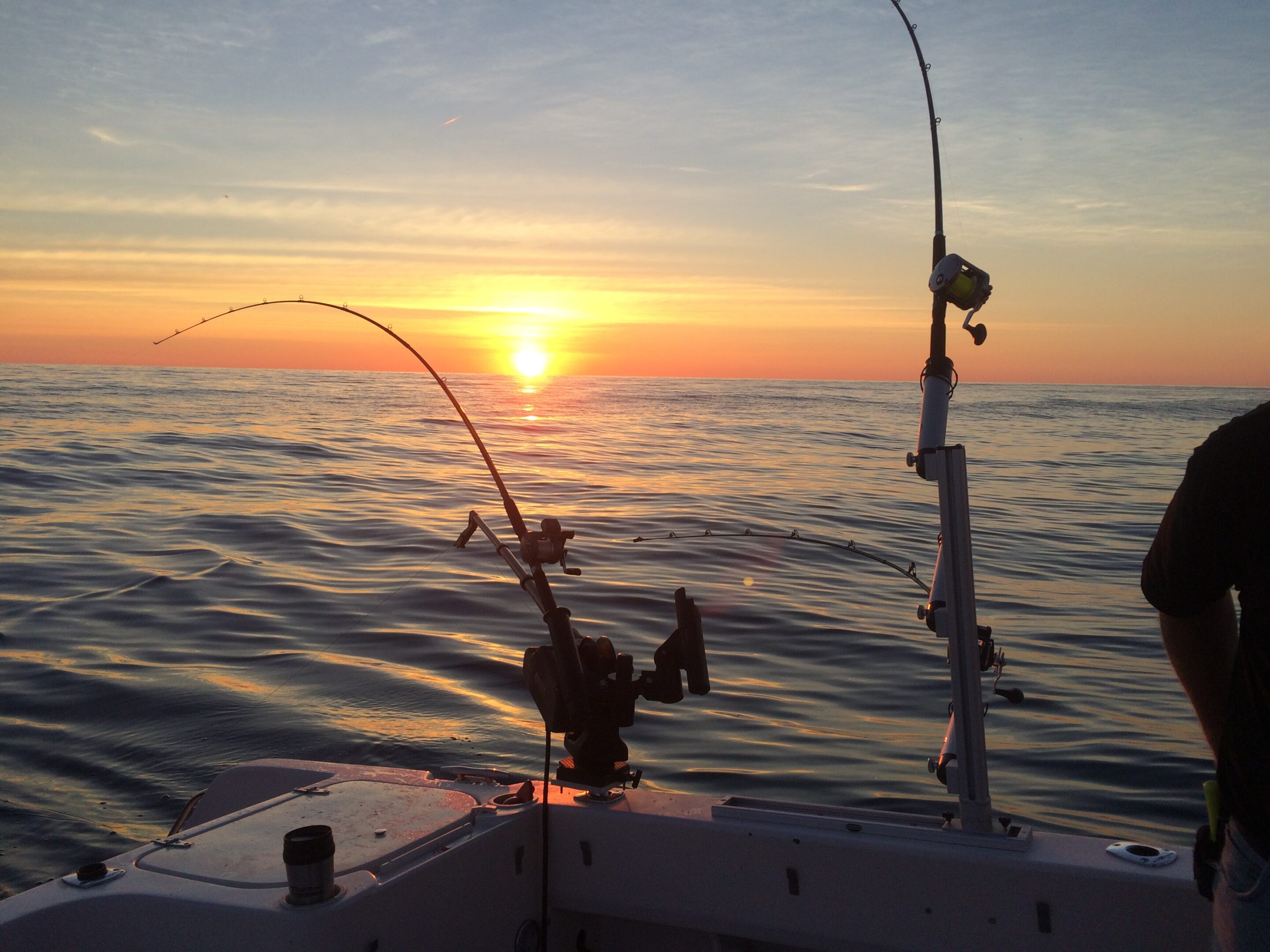 Fishing rods on a boat at sunset over calm waters.
