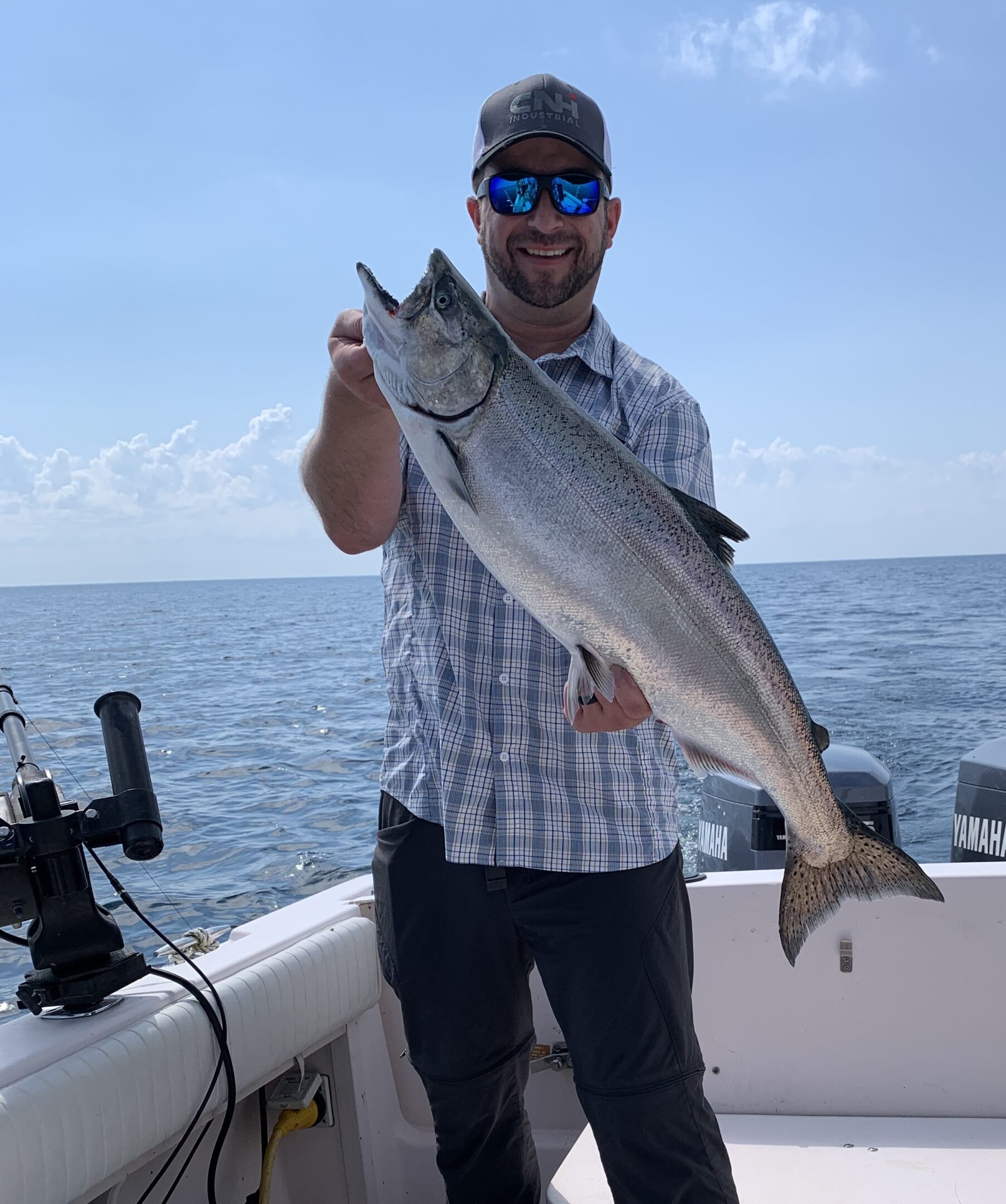 Man holding a large fish on a boat under a clear sky.