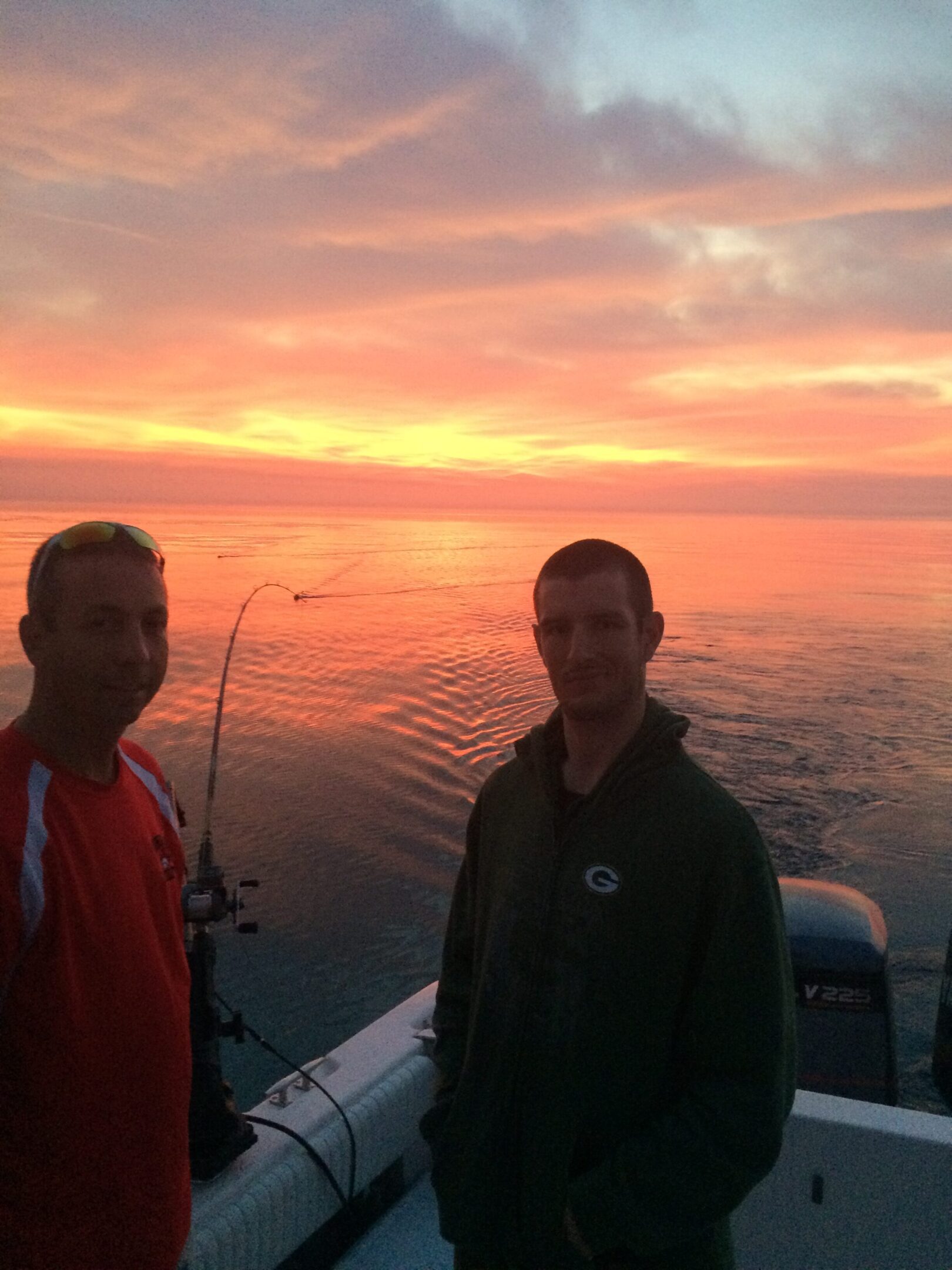 Two men fishing on a boat during sunset.