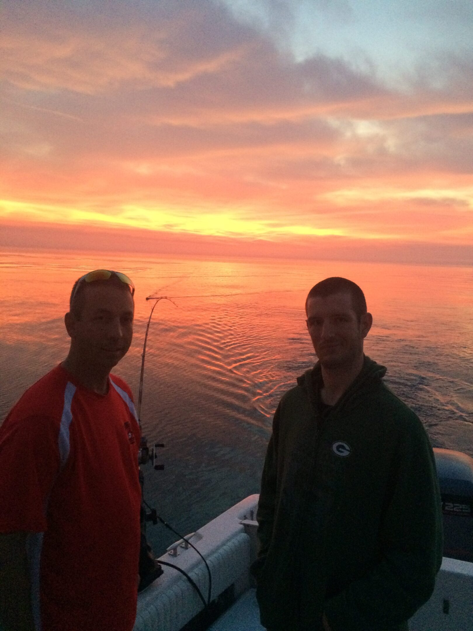 Two men standing on a boat at sunset with a calm sea.
