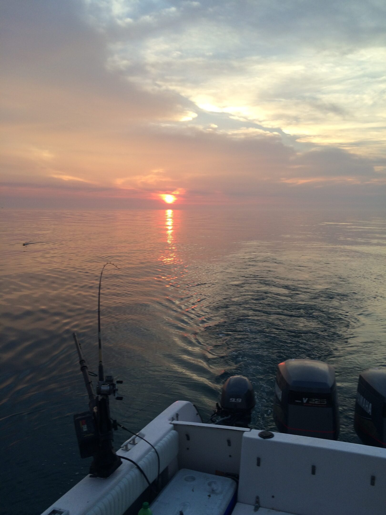 Sunset over calm waters with fishing rods on a boat.