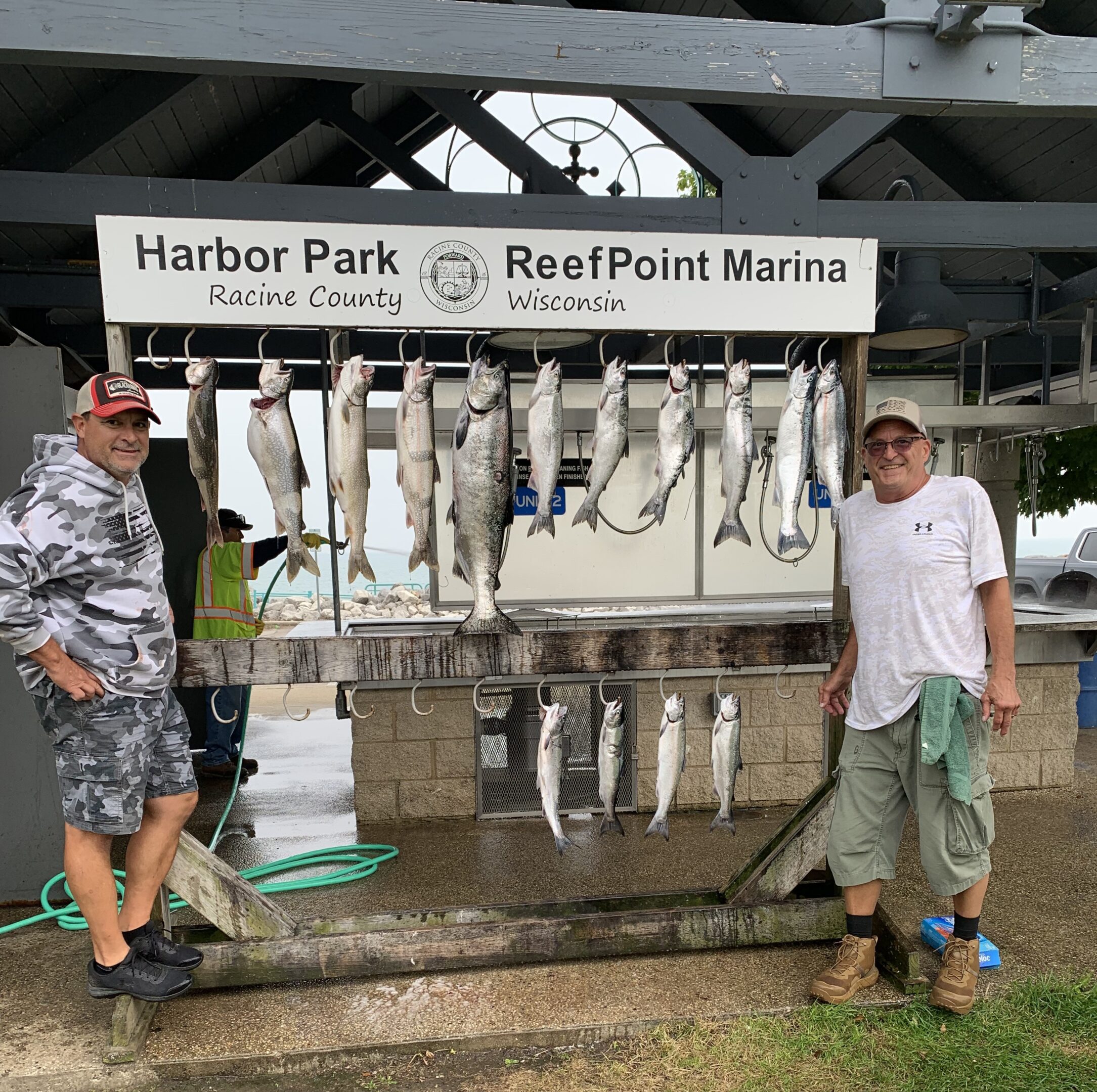 Two men standing beside a display of large fish at a marina.