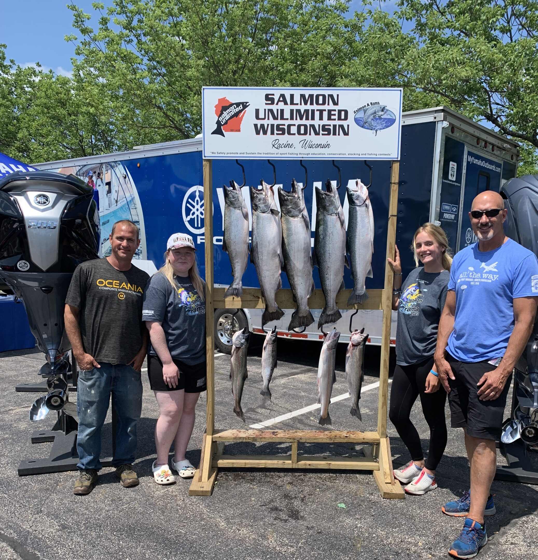 Five large fish hanging on display with four people posing nearby outdoors.