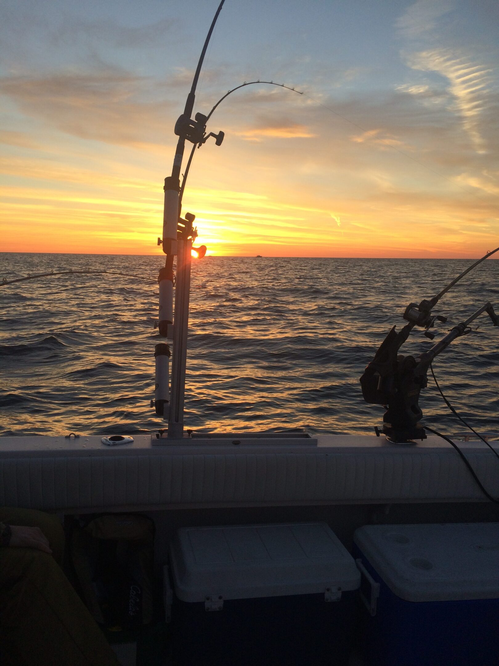 Fishing rods on a boat at sunset over the ocean.