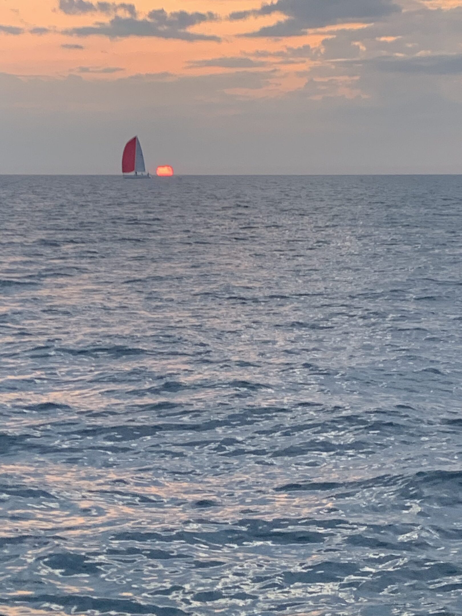 A sailboat with a red and white sail on the ocean at sunset.