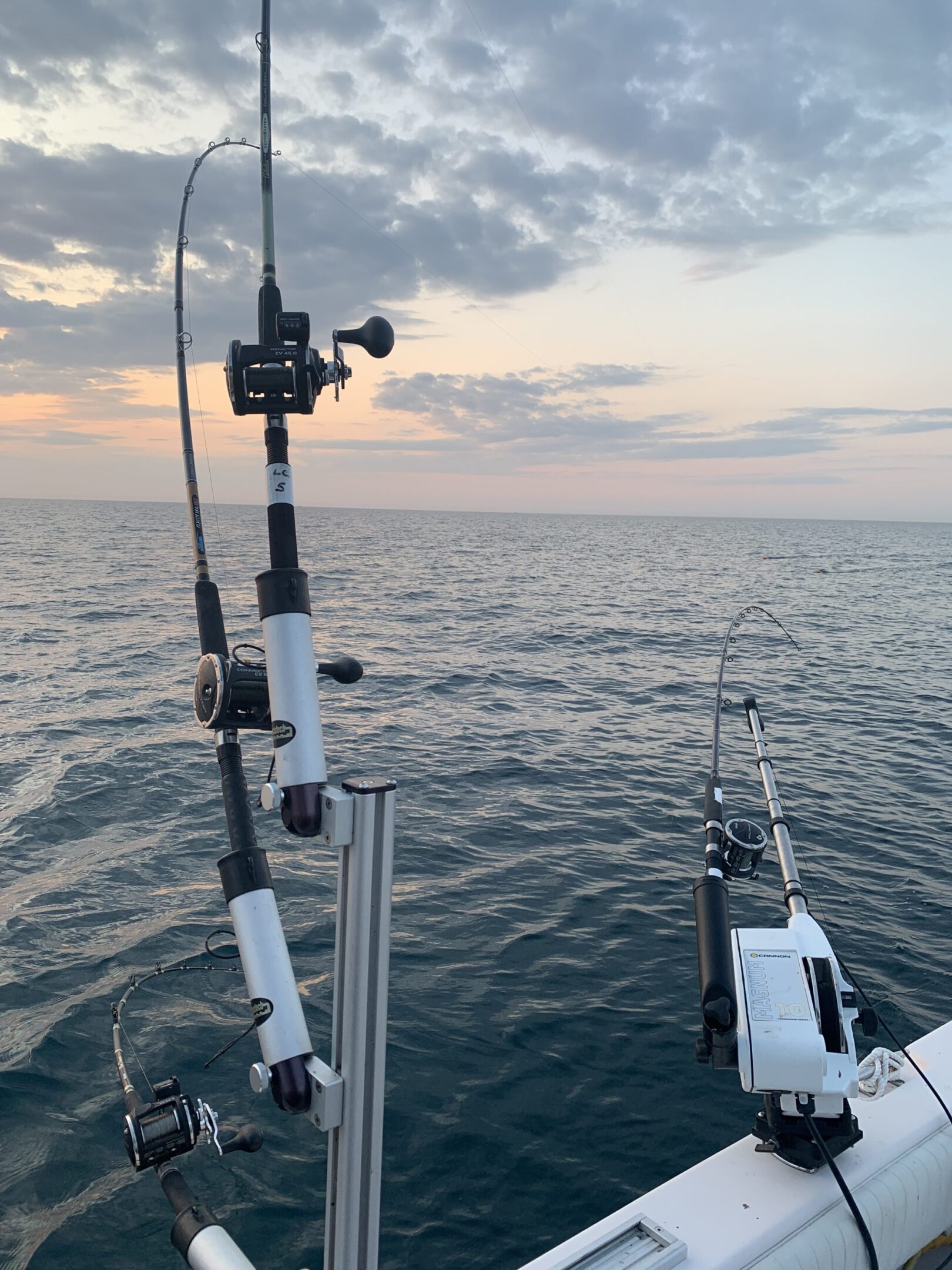 Fishing rods set up on a boat at sea during sunset.