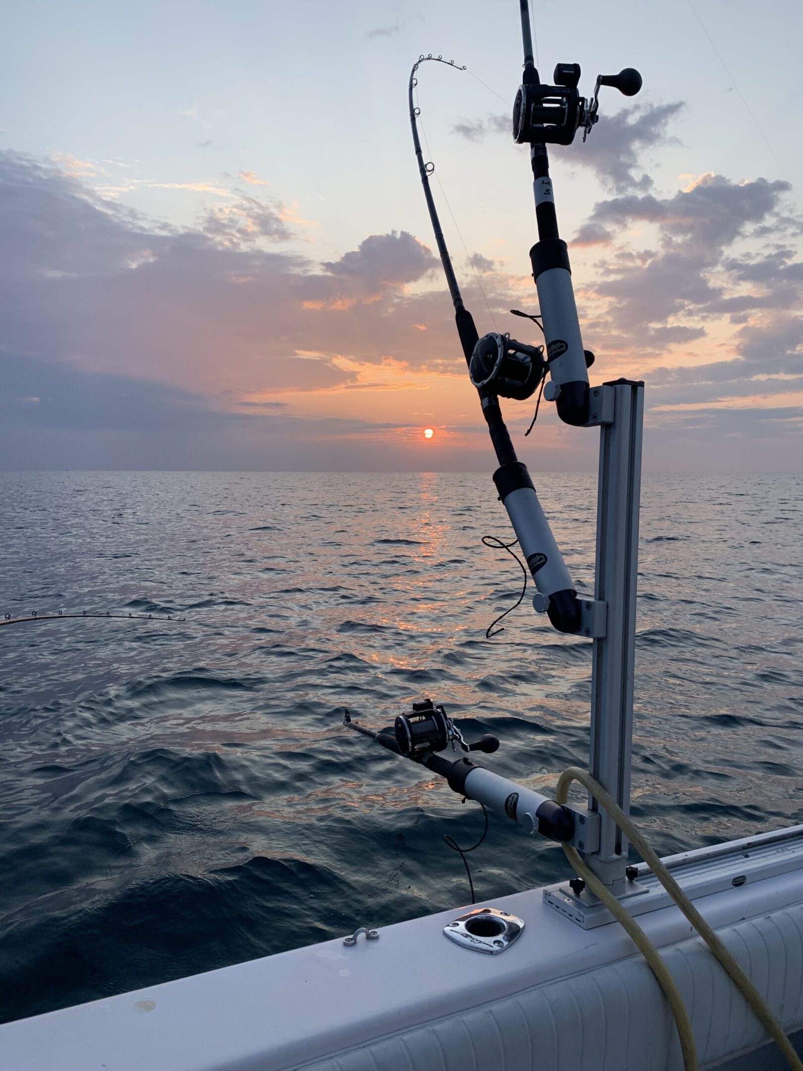 Fishing rods on a boat at sunset over the ocean.