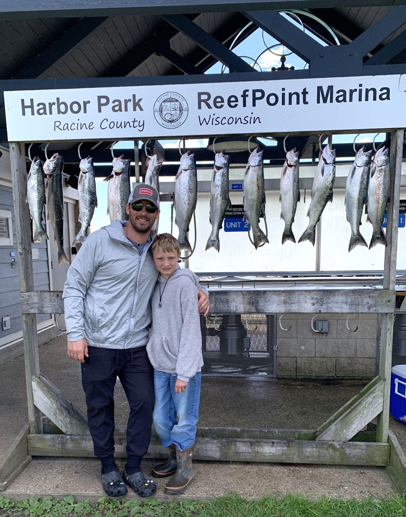 A man and a boy posing with their catch of fish at a marina.