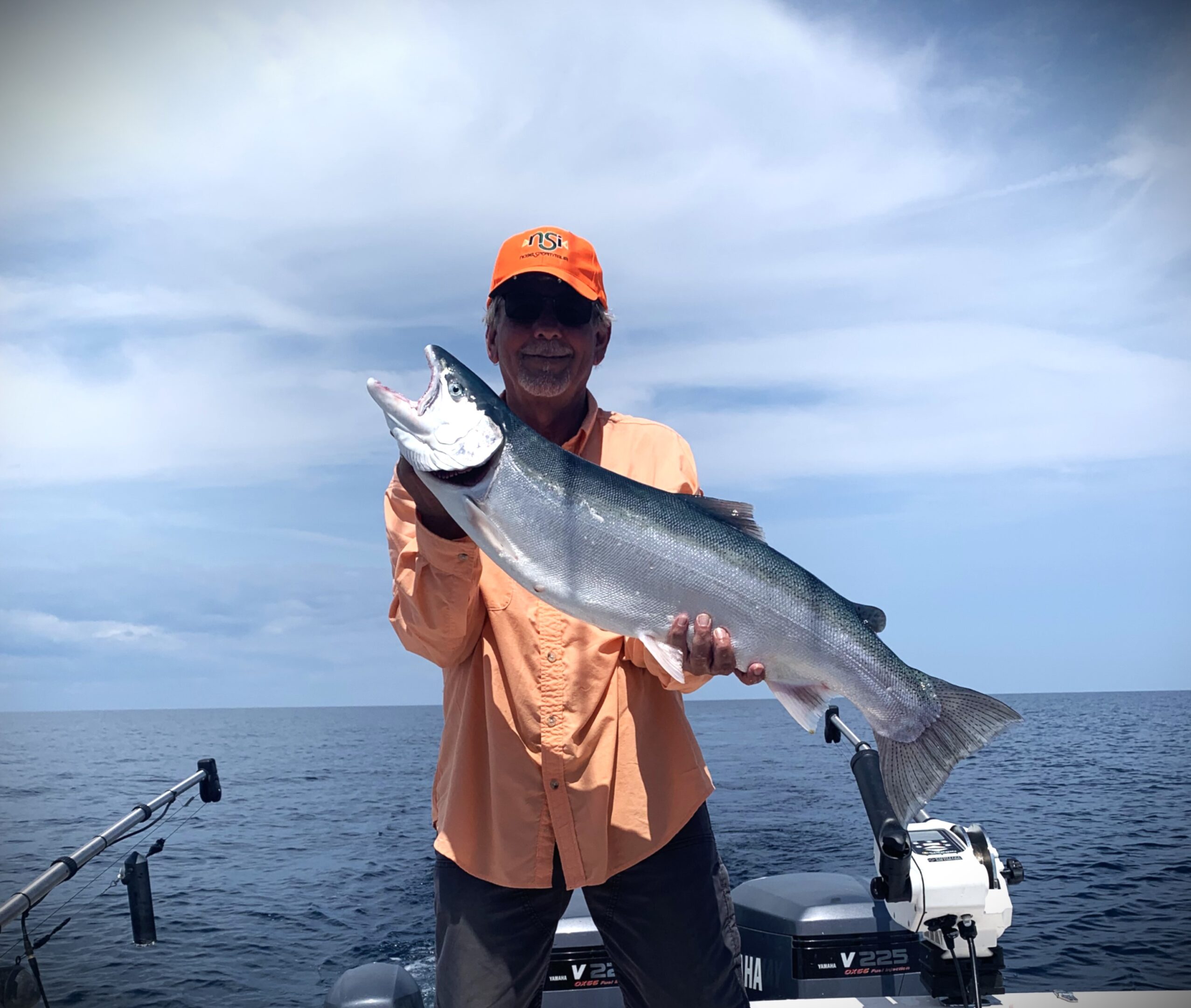 Person holding a large fish on a boat under a cloudy sky.