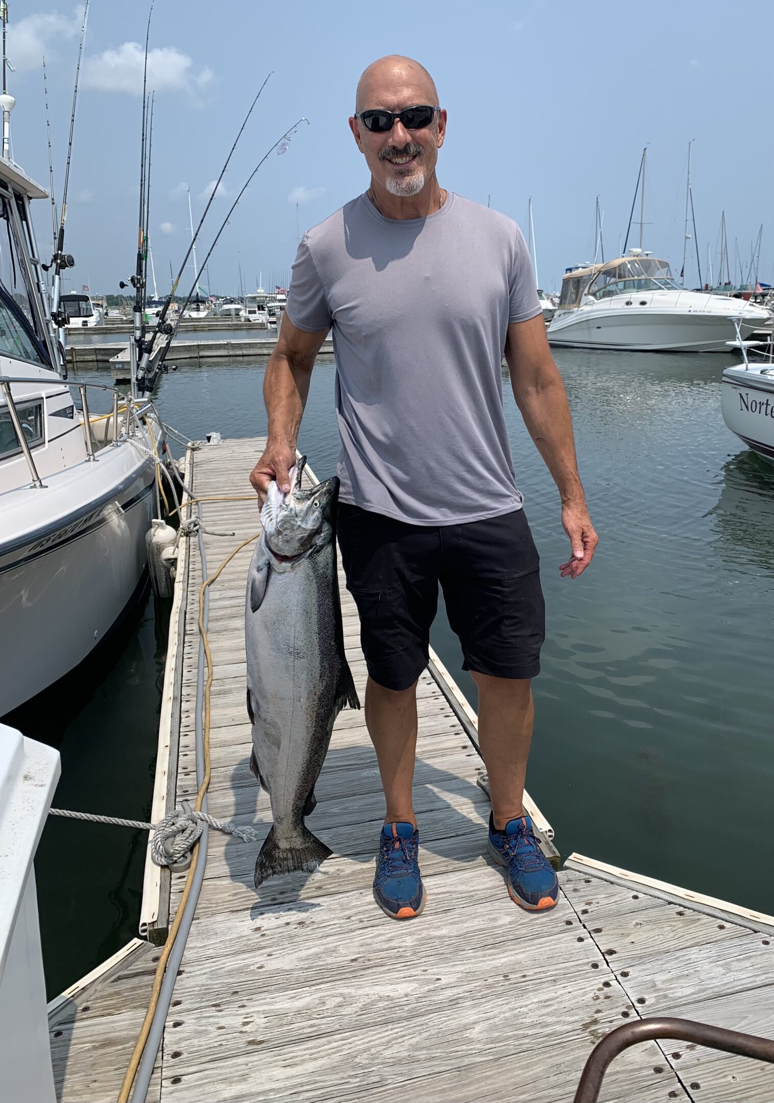 Man holding a large fish on a marina dock.