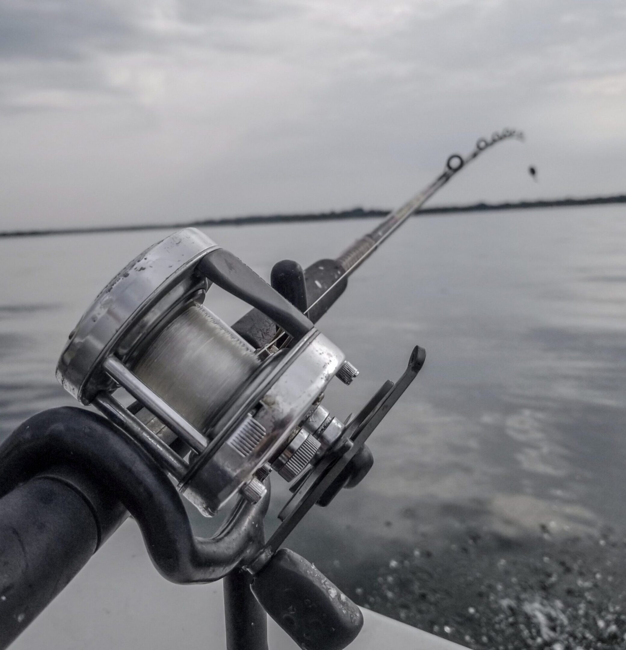 Fishing rod and reel mounted on a boat over calm water.