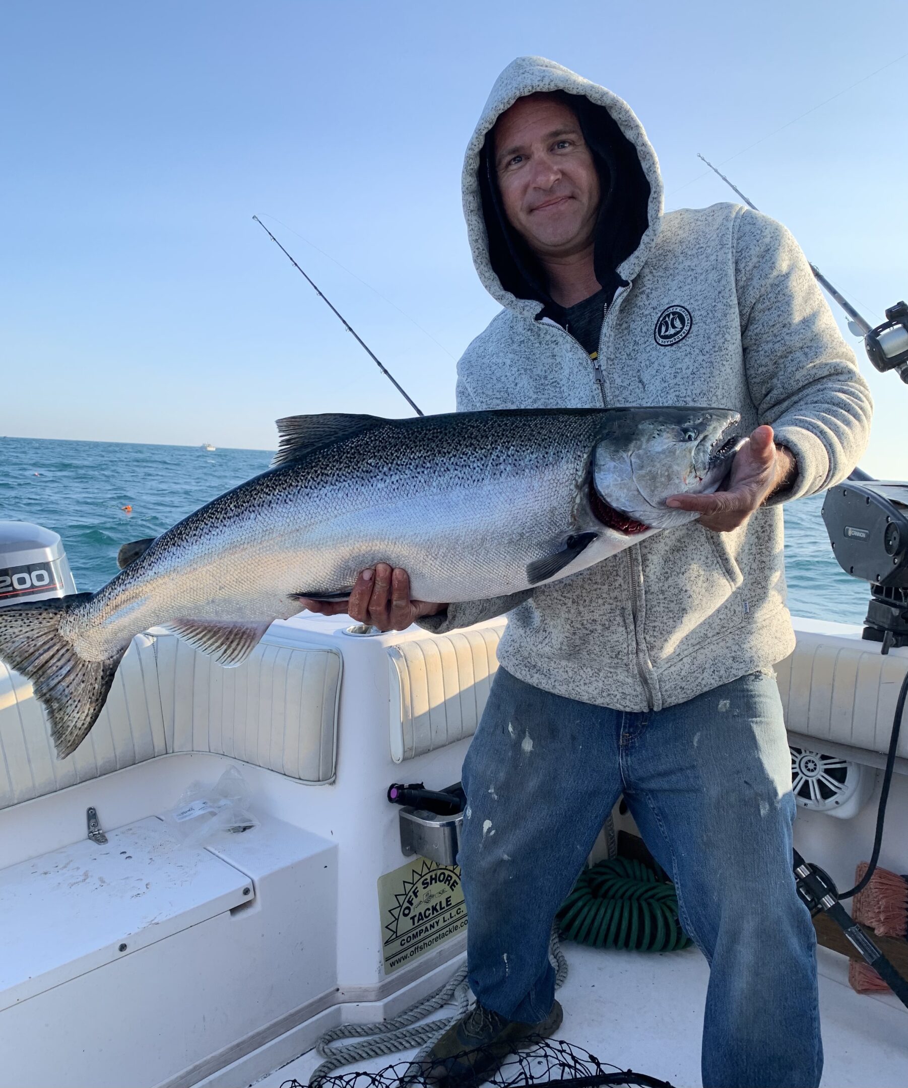 Person holding a large fish on a boat under clear skies.