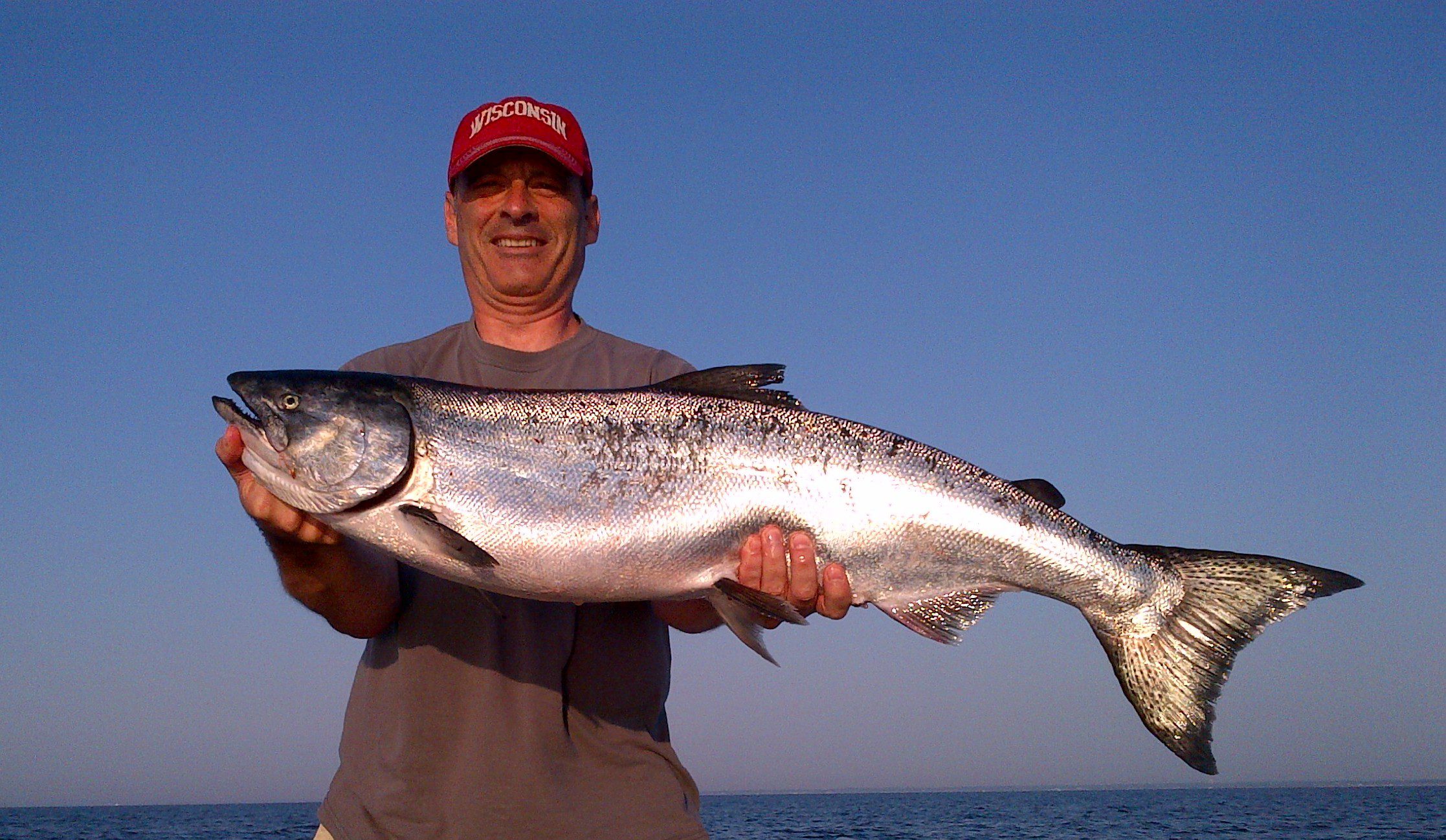 Man proudly holding a large fish against a clear blue sky.