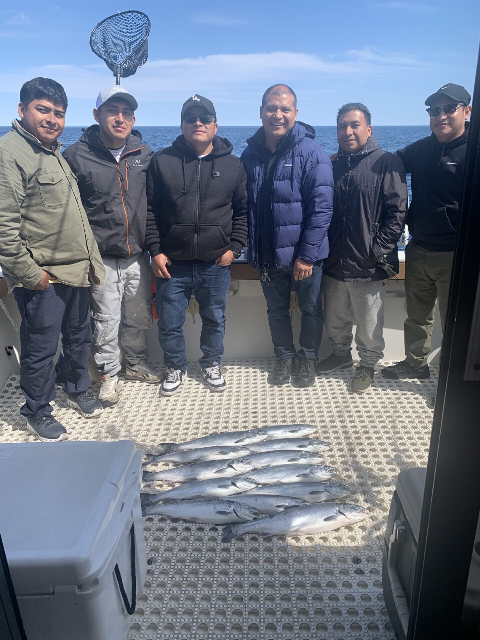 Group of men posing with freshly caught fish on a boat.