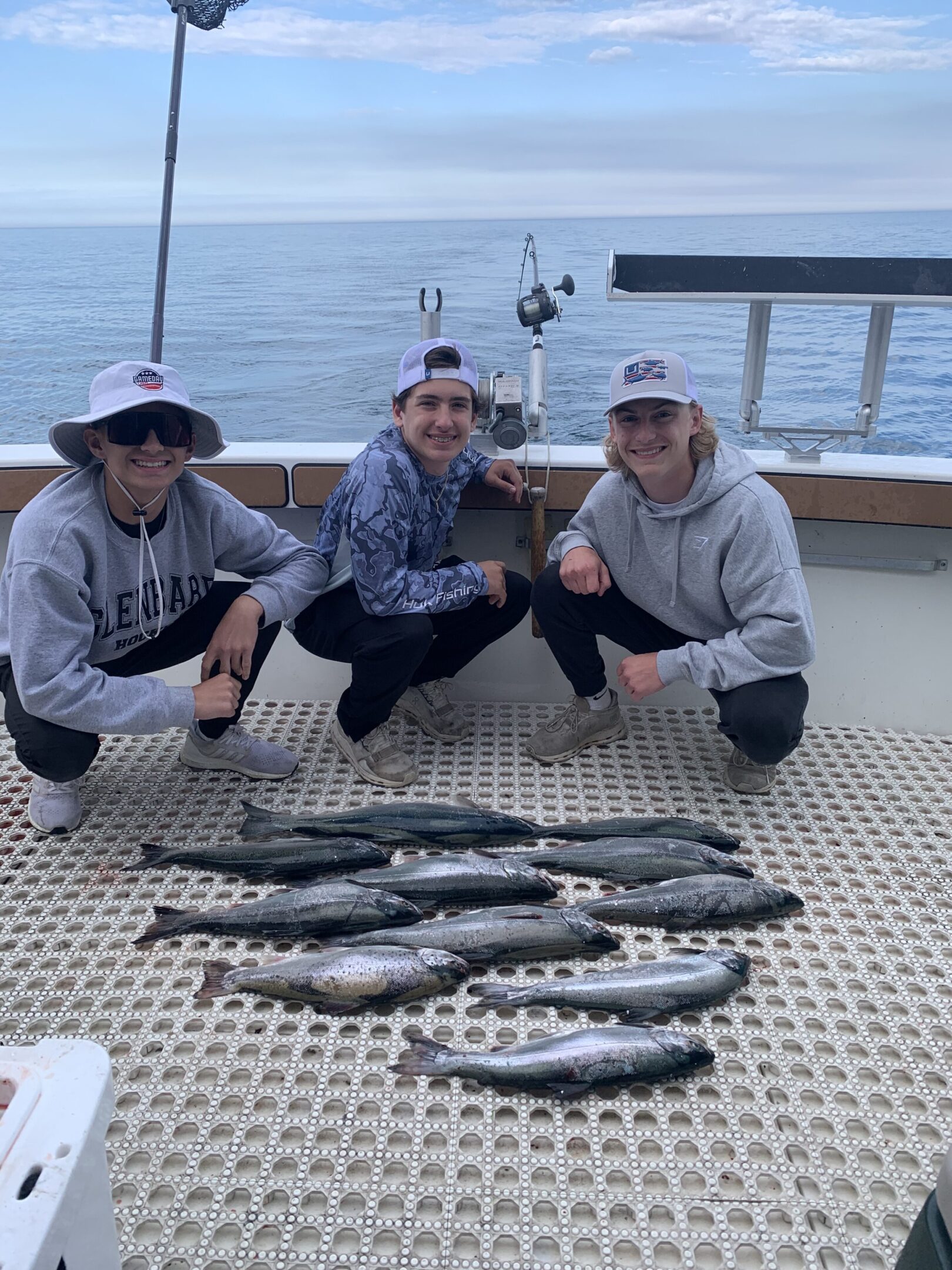 Three people posing with freshly caught fish on a dock by the water.
